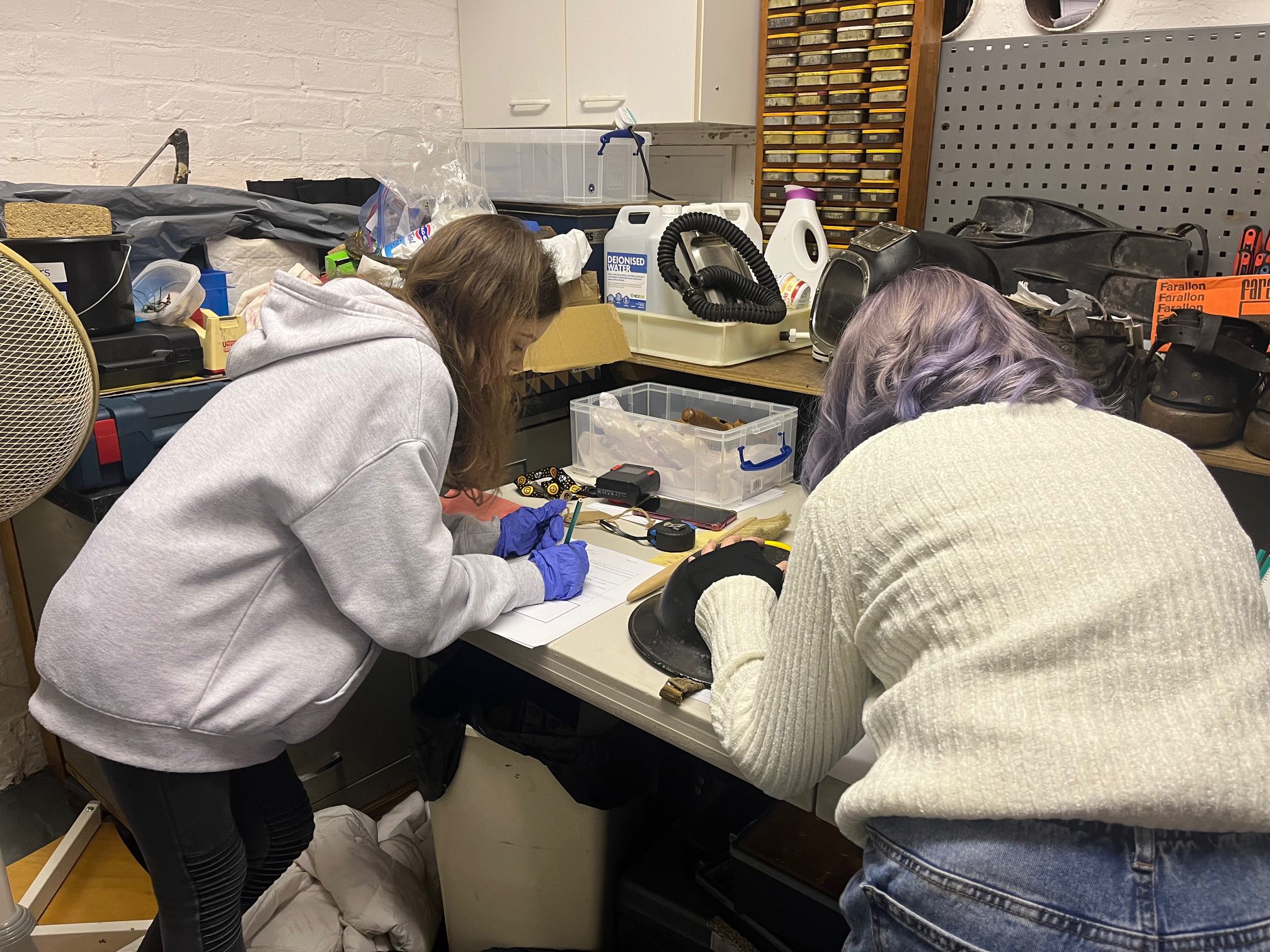 Two young people in a workshop surrounded by old diving equipment and tools to clean objects