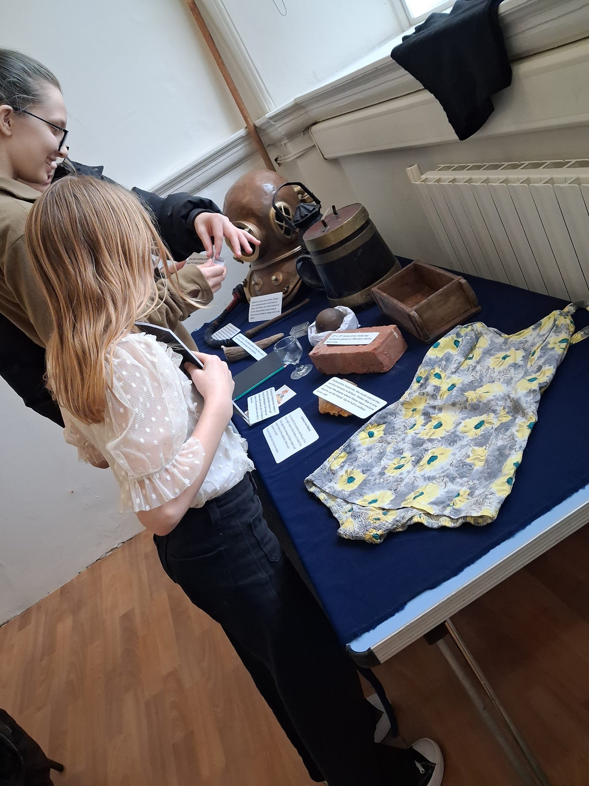 Young people looking at a table of objects including an old swimming costume, brick and brick mould